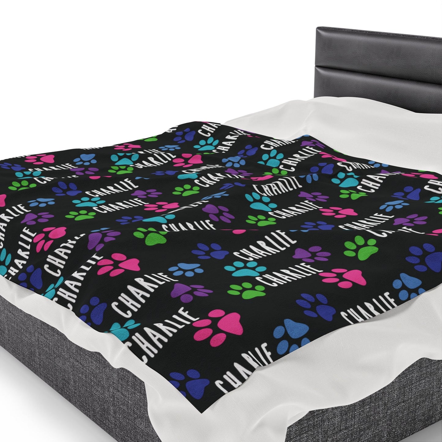 a bed with a black blanket with colorful paw prints