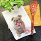 a picture of a dog with a pink bow tie on a napkin next to a